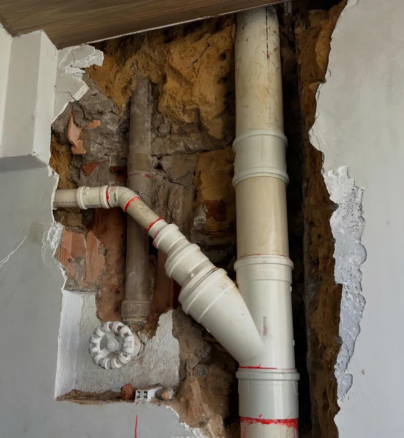 Parede aberta com prumada hidráulica e tubulação expostas antes do reparo